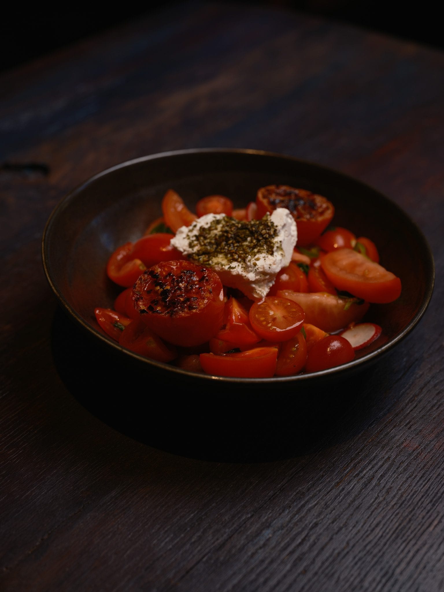Three tomato salad at GUSI with feta, herbs, and cracked pepper in a dark bowl